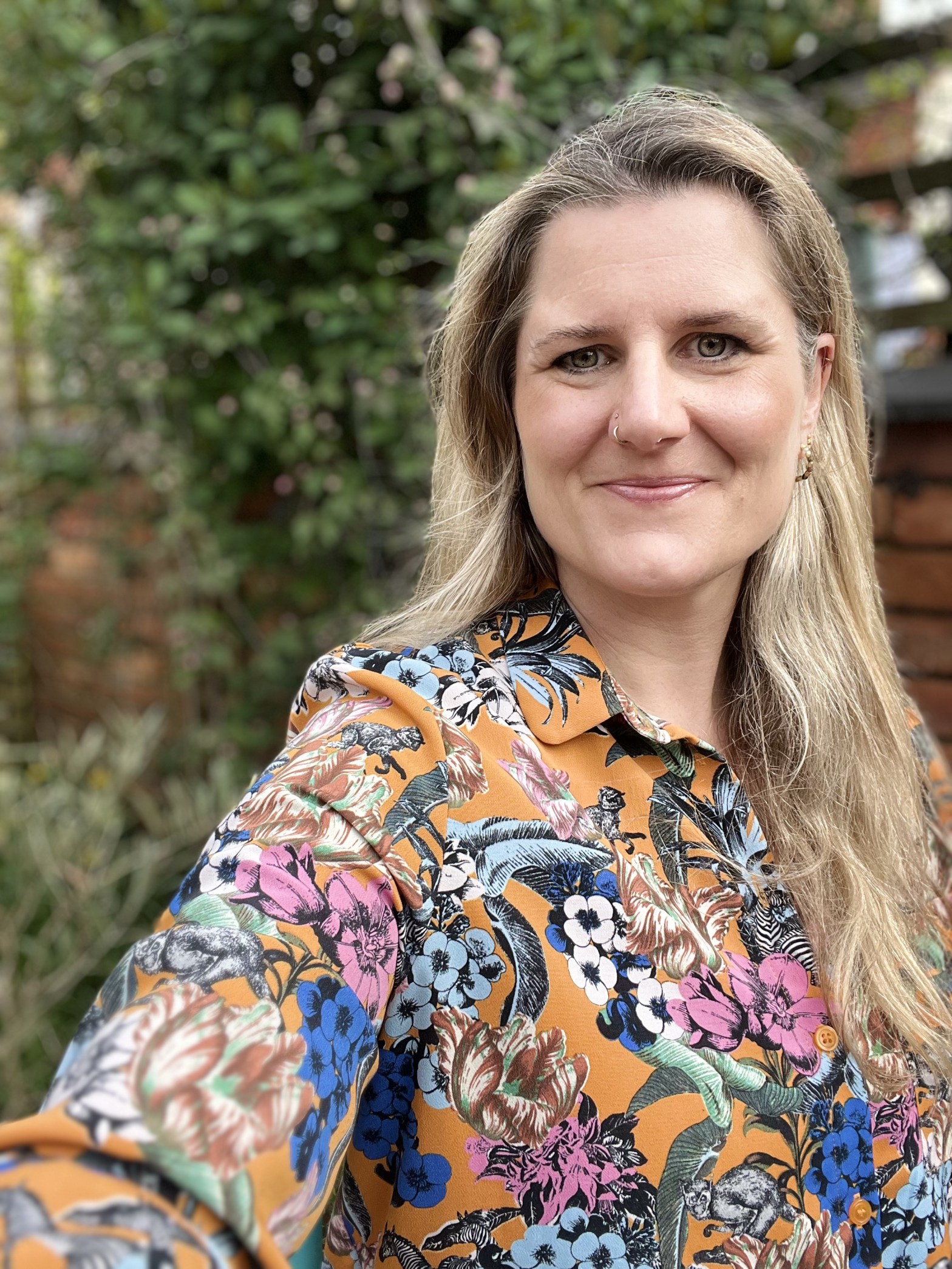 Laura Hamblyn in the garden, smiling, wearing and orange patterned shirt